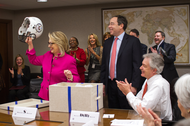 Clinton holds up a football helmet — a gift from her staff. Her clot was discovered after a fall and concussion.