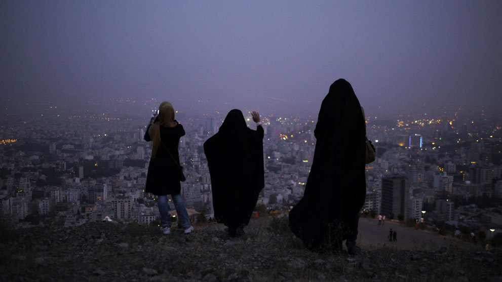 Women in the hills above Tehran at dusk. Concealing clothing in the Islamic Republic, including head coverings, is mandatory for women, but the exact definition of «modest» is flexible, leading to a tug of war between young females and the authorities each spring. Outside metro stations female police can be seen regularly checking the passers by. If a woman's dress is considered «immodest» she is arrested and taken into custody. In 2010 a senior cleric in Tehran blamed the frequency of earthquakes in Iran on women who «lead young men astray» with their revealing clothing.