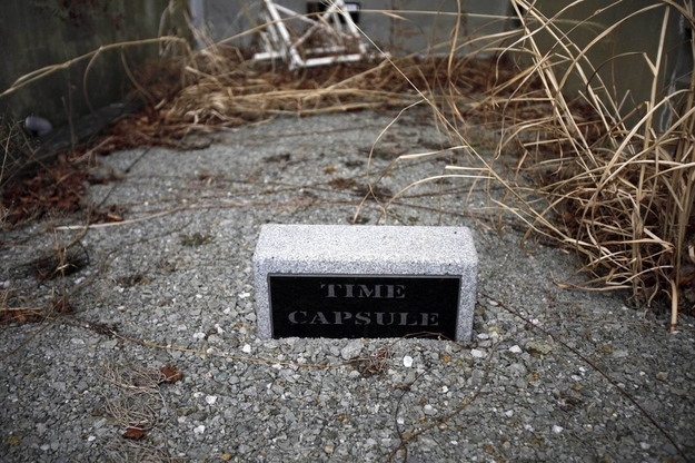 A time capsule is surrounded by weeds at the school.