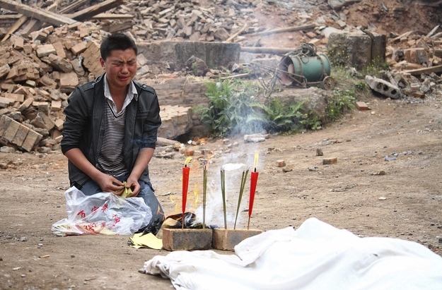 A man cries as he burns offering in front of the body of his relative.