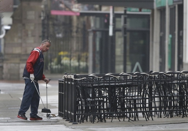 A man sweeps around the outdoor seating area at a Boylston business on Tuesday, when businesses near the finish area were preparing to re-open.
