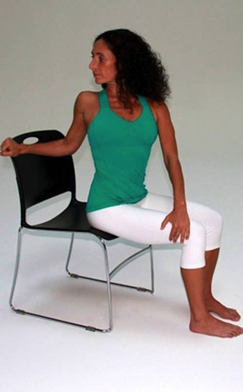 Sit on the edge of your chair with your feet firmly planted on the floor. Hold the back of the chair with one hand put the other hand on the outside of the opposite knee. Twist your torso in the direction of your hands.