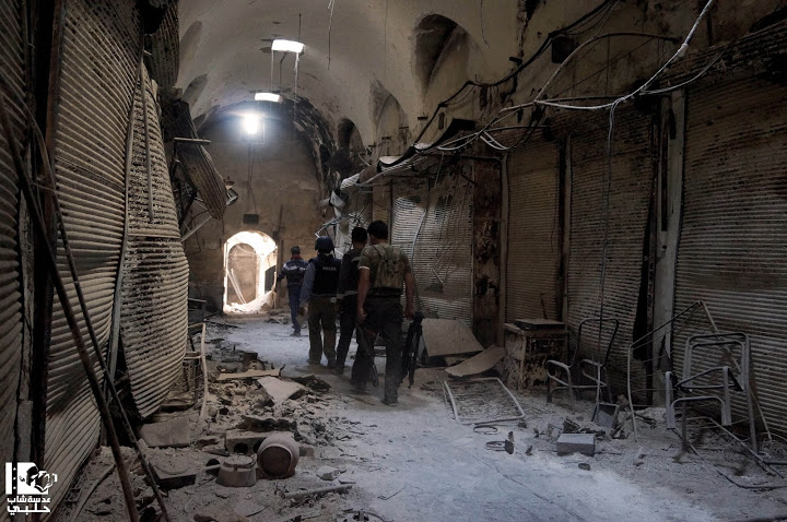 Press and rebel fighters inspect a destroyed market in Aleppo.