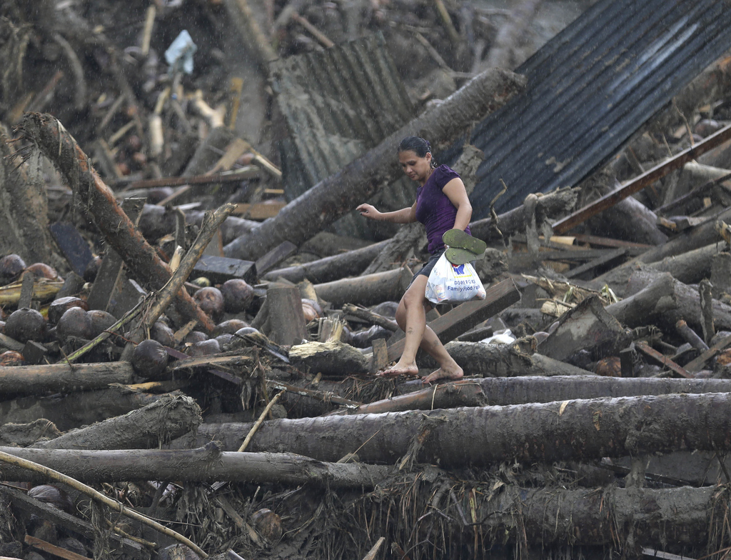 A resident walks back home with a plastic bag of relief goods amidst the debris from Tuesday's Typhoon Bopha at New Bataan township, Compostela Valley in southern Philippines, Dec. 7, 2012.