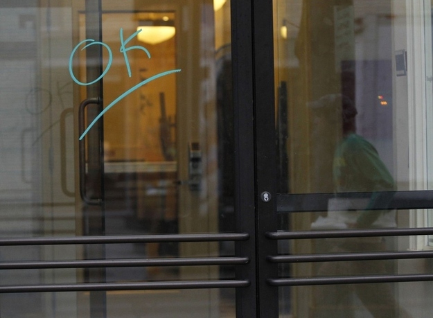 A person is reflected in a glass door with the word "OK" scrawled on it.