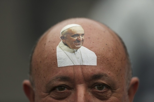 A Catholic faithful with a sticker bearing an image of Pope Francis on his forehead waits for the pope to arrive at the beach.