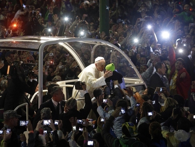 Pope Francis reaches out from his popemobile to kiss a child as he makes his way through the crowds lining the Copacabana beachfront.