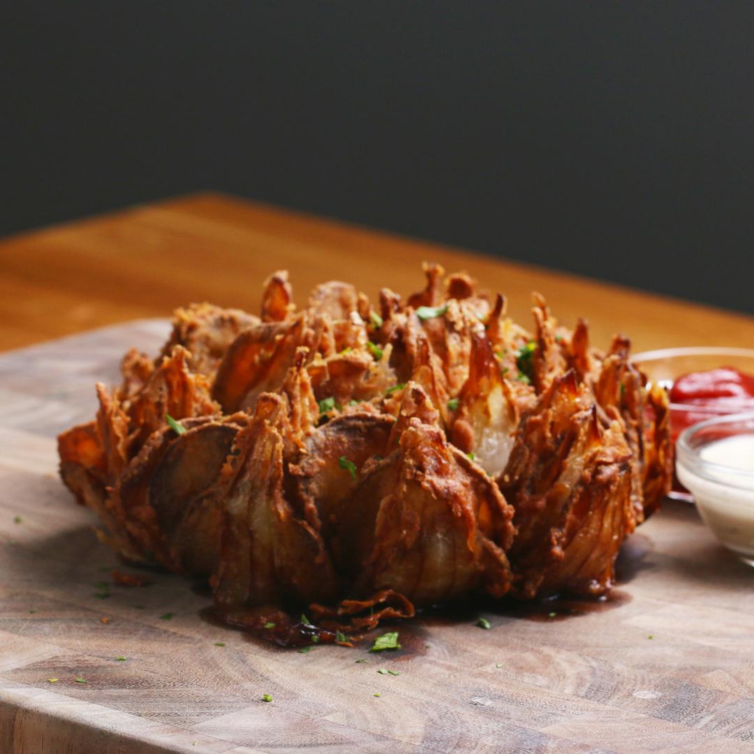 Crispy blooming onion served on a wooden board with dipping sauces on the side