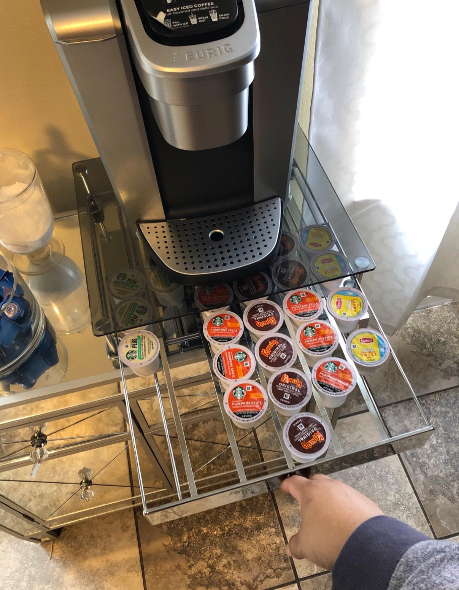 Reviewer pulling out a glass top keurig pod organizer stashed underneath a large keurig machine 