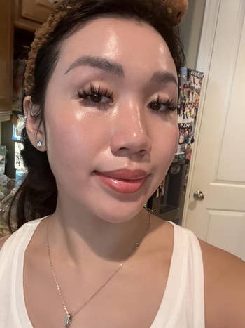 A idiosyncratic   with glossy tegument  and agelong  eyelashes, wearing a sleeveless apical  and a necklace, poses indoors with a flimsy  smile
