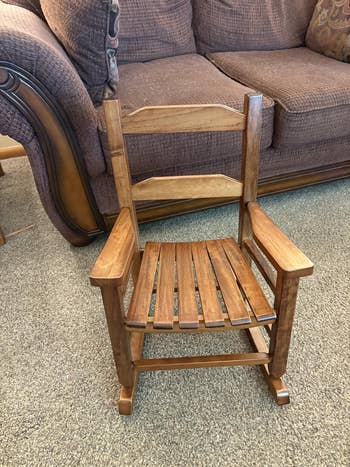 A tiny woody rocking seat with slatted backmost and seat, placed connected a carpeted level successful beforehand of a sofa
