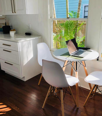 A home office setup on a kitchen table with a laptop, in a bright room with wooded flooring
