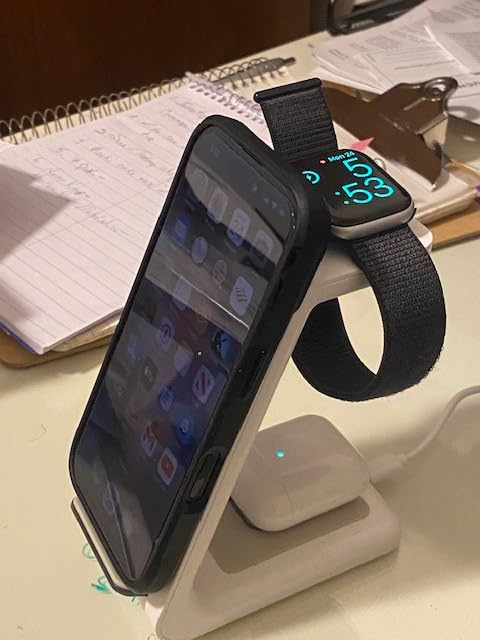 Smartphone and smartwatch on a charging stand, showing time. A clipboard and notebook with notes in the background