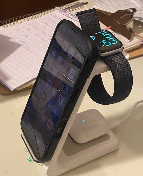 Smartphone and smartwatch on a charging stand, showing time. A clipboard and notebook with notes in the background