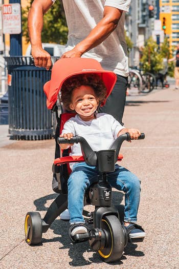model pushes a smiling child in a red trike
