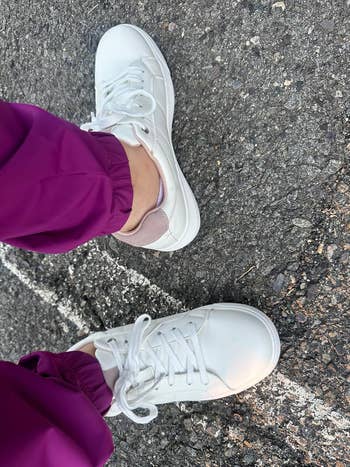 Person wearing white sneakers with purple pants, shown from above on a pavement