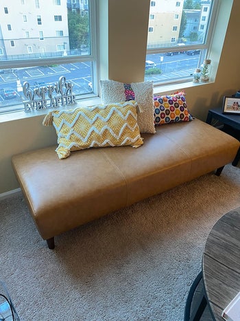 reviewer photo of long rectangular brown leather ottoman by a window