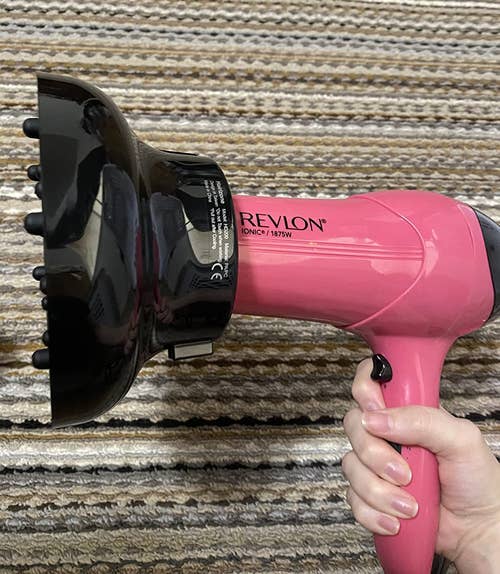 a reviewer holding a pink blow dryer with the diffuser attached 