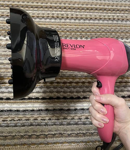 a reviewer holding a pink blow dryer with the diffuser attached 