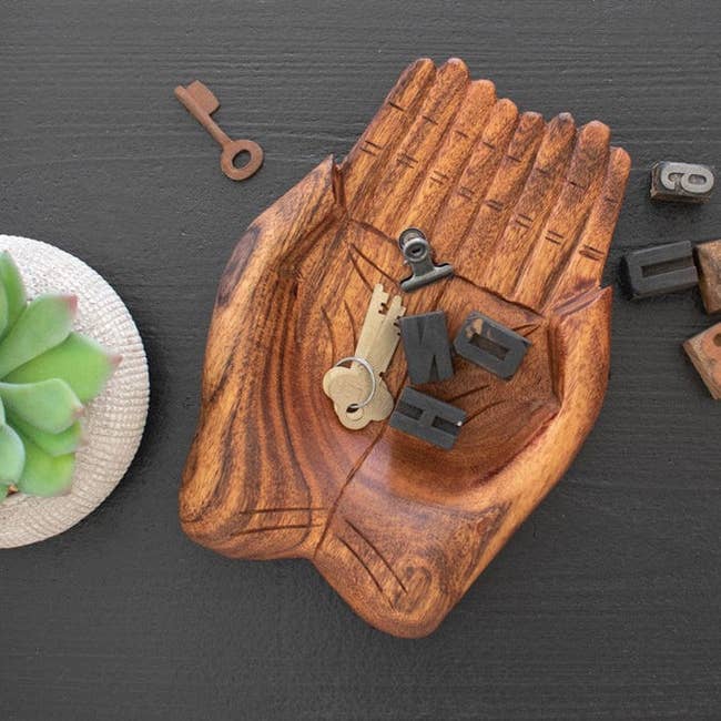 Wooden hand-shaped dish holding keys, next to succulent and letter blocks
