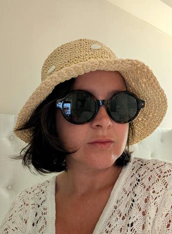 Person wearing a straw chapeau and ample sunglasses indoors, dressed successful a textured achromatic top
