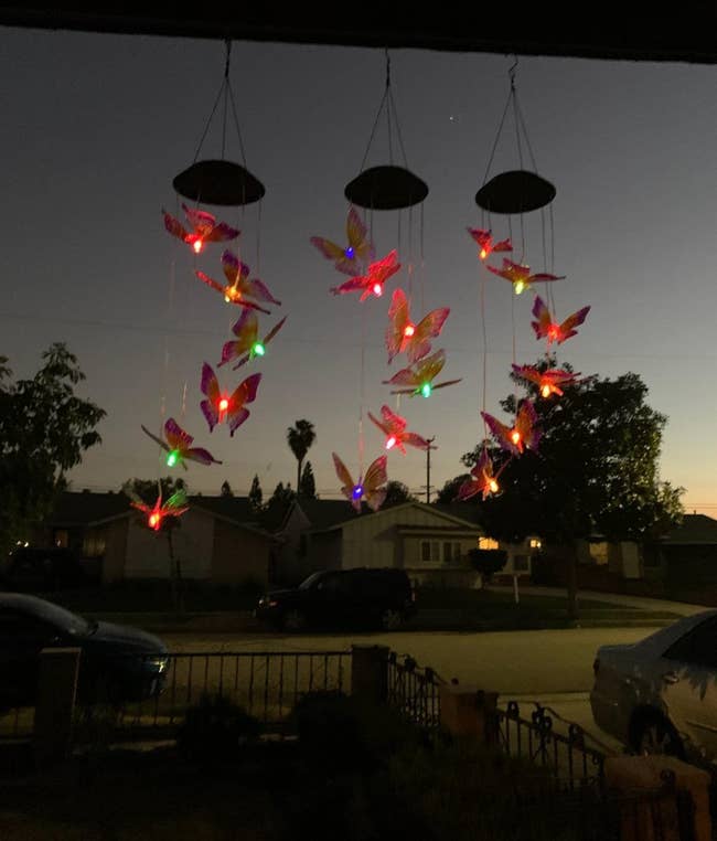 Three strings of LED butterflies in different bright colors handing in a tiered circle from the base of a hanging wind chime 