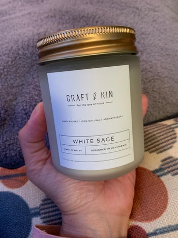 Reviewer holding white candle jar that reads 