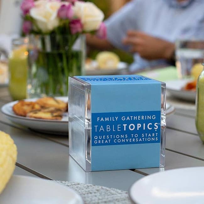 TableTopics question container connected a eating table, surrounded by nutrient and flowers, designed to animate engaging household conversations