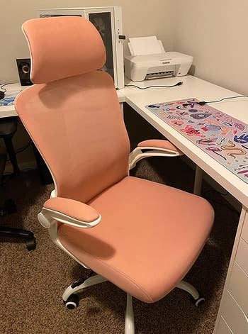 a reviewer photo of the same chair in pink sitting in front of a desk 