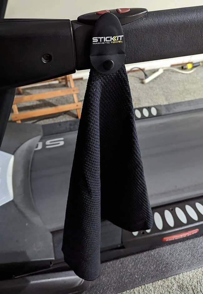 reviewer photo of the black towel hanging from a treadmill by the magnet