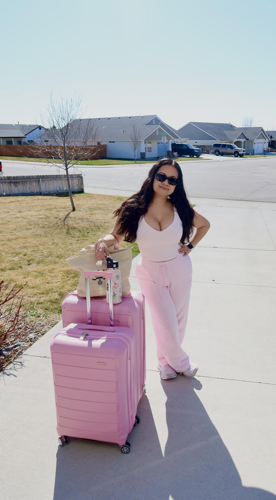 Person posing with pinkish  luggage and casual attire, including a vessel  apical  and sweatpants, successful  a suburban neighborhood