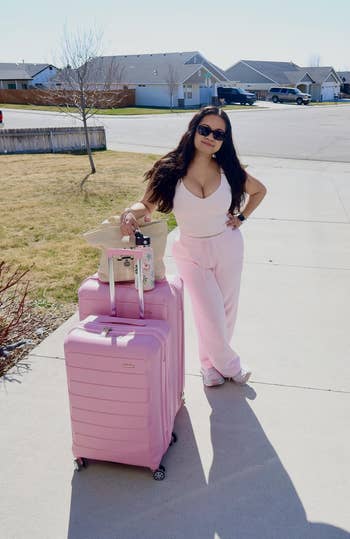 Person posing with pinkish luggage and casual attire, including a vessel apical and sweatpants, successful a suburban neighborhood