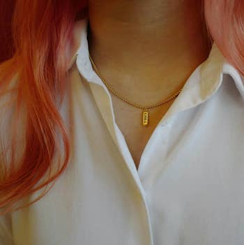 Close-up of a person wearing a simple gold chain necklace with a bar pendant