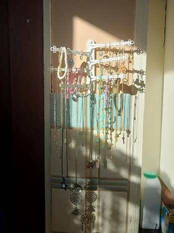 Jewelry organizer with assorted  necklaces and bracelets, including beads and pendants, hanging by a window