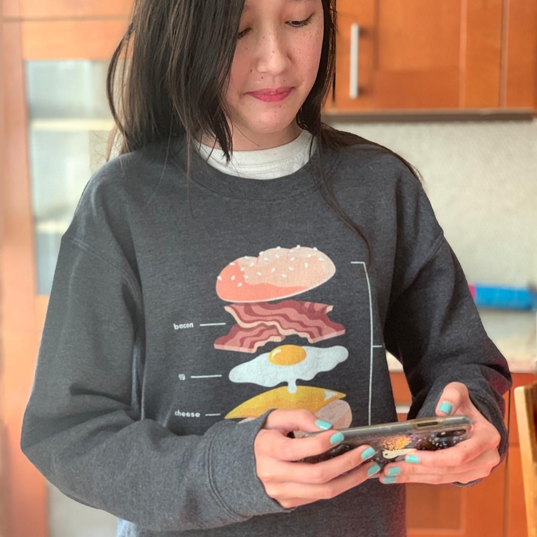 person wearing a soft gray crewneck sweatshirt with a breakfast sandwich diagram on it