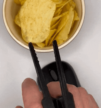 Model wearing a small chopstick-like device between two fingers and plucking a chip out of a bowl with it 