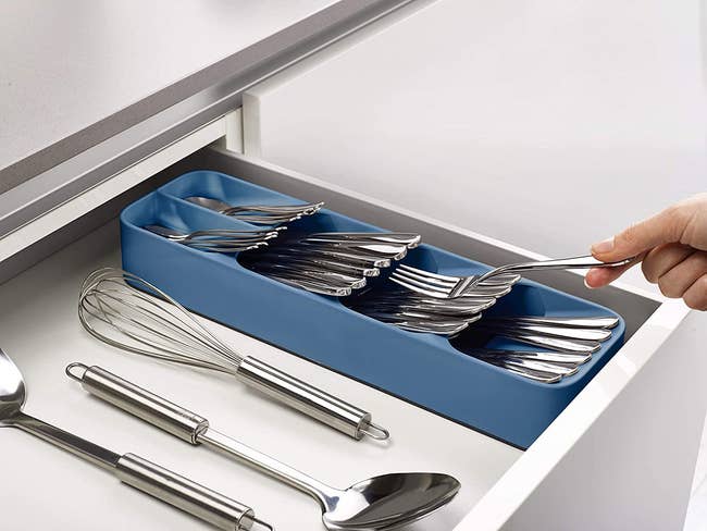 A blue rectangular organizer in a shelf that a model is sliding cutlery into 