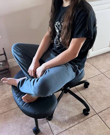 Person seated cross-legged on ergonomic office chair in a home setting, wearing casual loungewear