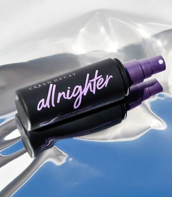 the black bottle of setting spray with purple writing on a reflective surface