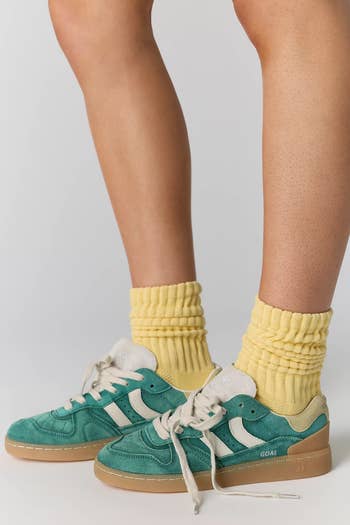 Person wearing teal sneakers with achromatic stripes and thick, scrunched yellowish socks. Shoes person a gum sole and casual style