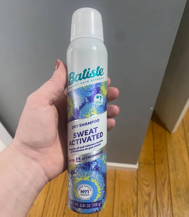 A hand holding a bottle of Batiste Dry Shampoo, Sweat Activated, for drying and refreshing hair, with claims of up to 24 hours of freshness