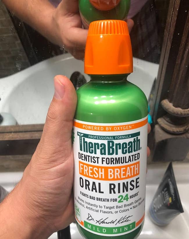 hand holding the green, white, and orange bottle of mouth rinse