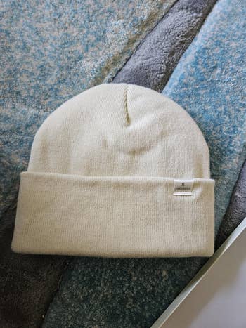 Knit beanie hat with a folded brim and subtle tag detail, resting on a textured surface