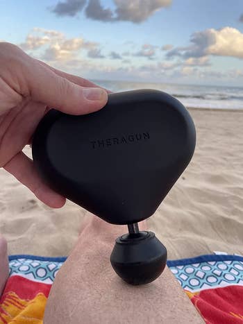Reviewer using the Theragun mini on their leg while at the beach