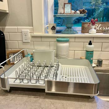 Dish rack on a kitchen counter holding no dishes, with soap and decor in the background
