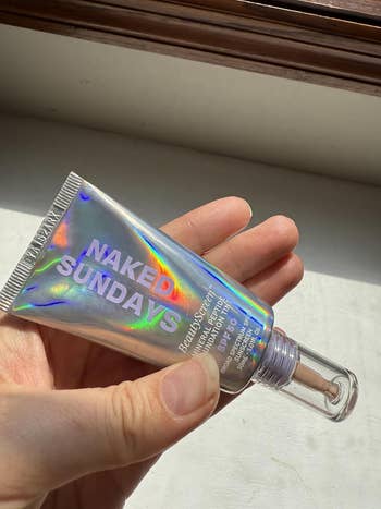 Person holding a conduit of Naked Sundays sunscreen gel SPF50 with holographic packaging