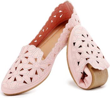 close up of a pair of pink cut-out floral design flats with one folded to show flexibility