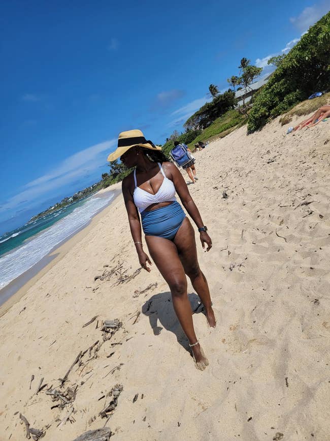 Person successful  stylish swimsuit and prima   chapeau  walking connected  a sandy formation  with the water  successful  the background
