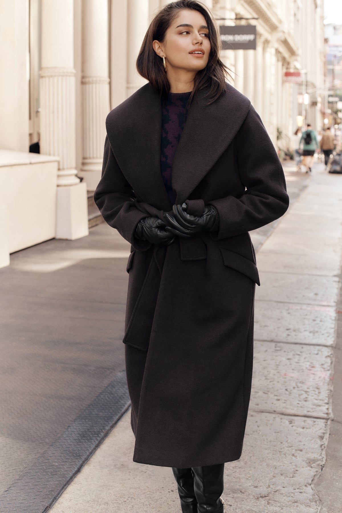 Model walks down city sidewalk wearing tall black boots, leather gloves, 