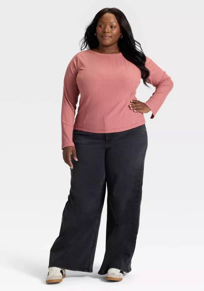 Woman models casual long-sleeve apical  with wide-leg pants and sneakers, hands connected  hips, showcasing relaxed and modern   style